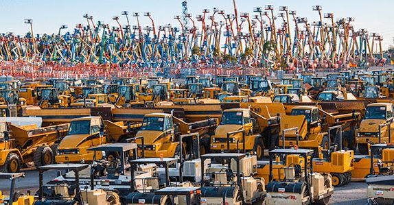 Ett stort fält fyllt med begagnade gula byggmaskiner och liftar.